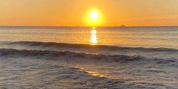 Sun setting over calm ocean waves with a warm glow.