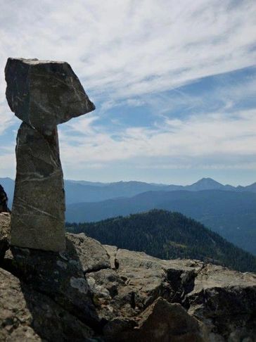 A tall, narrow rock formation stands on a mountain with a scenic view.
