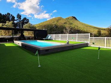 View of outdoor putting green with flags, elevated swimming pool, and covered braai area