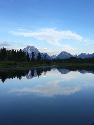 Snow topped mountains and tall trees reflect in a lake at Grand Tetons National Park