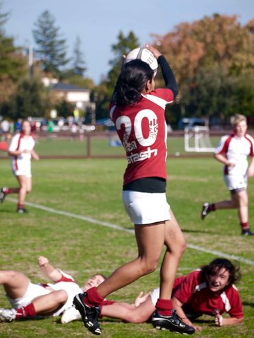 A Stanford Women's Rugby player catches a ball while other players look on