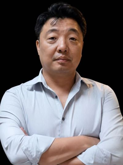 Man with arms crossed wearing a light blue shirt against a black background.