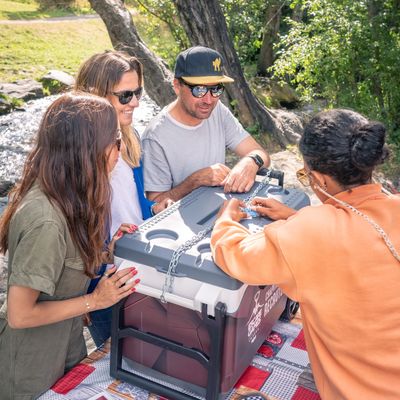 Four friends outdoors trying to unlock a chained box on a picnic table.