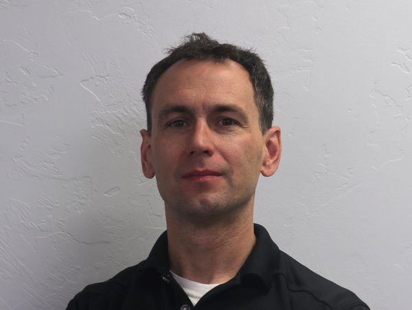 Man in black shirt standing against a white textured wall.