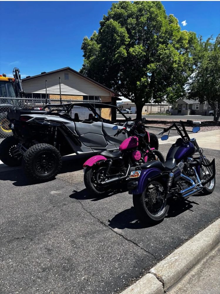 Two motorcycles and an off-road vehicle parked on a sunny day near a house and trees.
