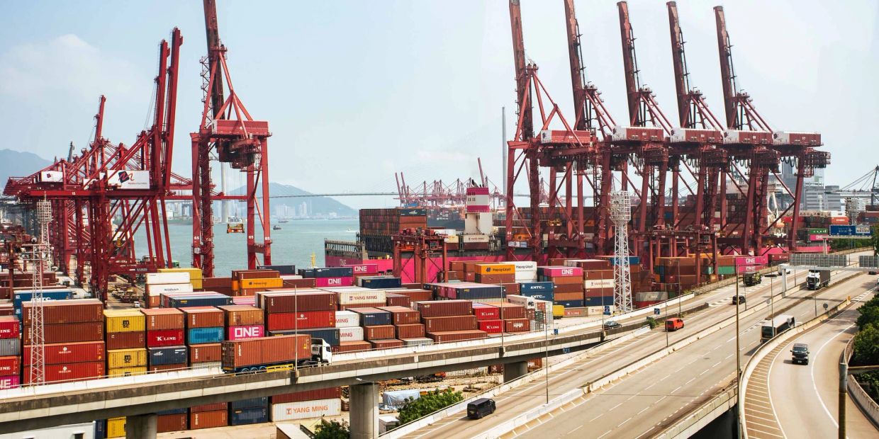 Busy port with red cranes and shipping containers.