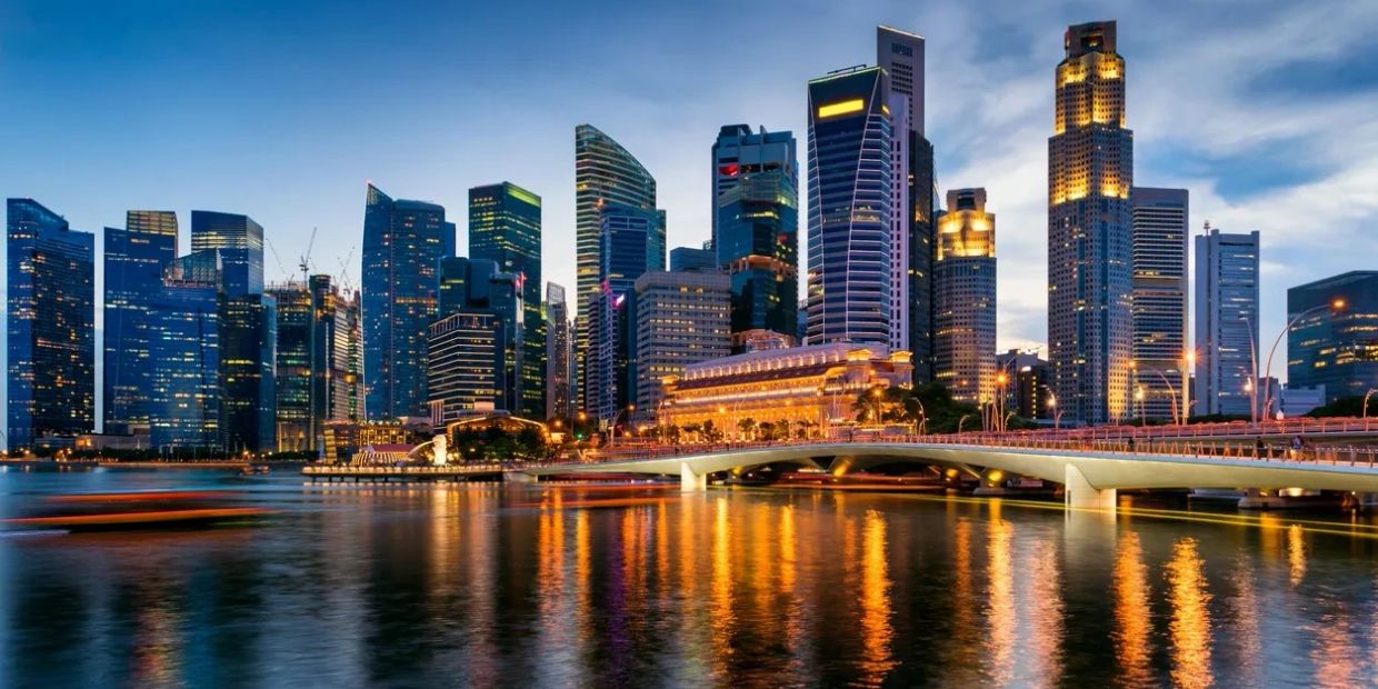 City skyline with illuminated skyscrapers reflecting on water at dusk.