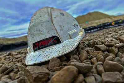 A dusty white hard hat lies on rocky ground under a cloudy sky.