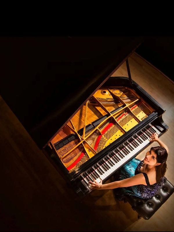 Woman playing a grand piano in a dimly lit room.