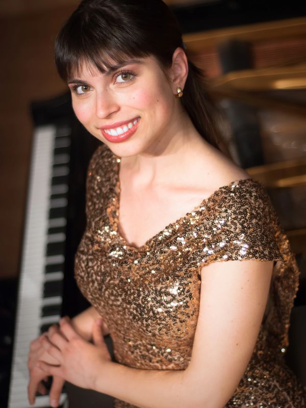Smiling woman in a sequined dress sitting at a piano.