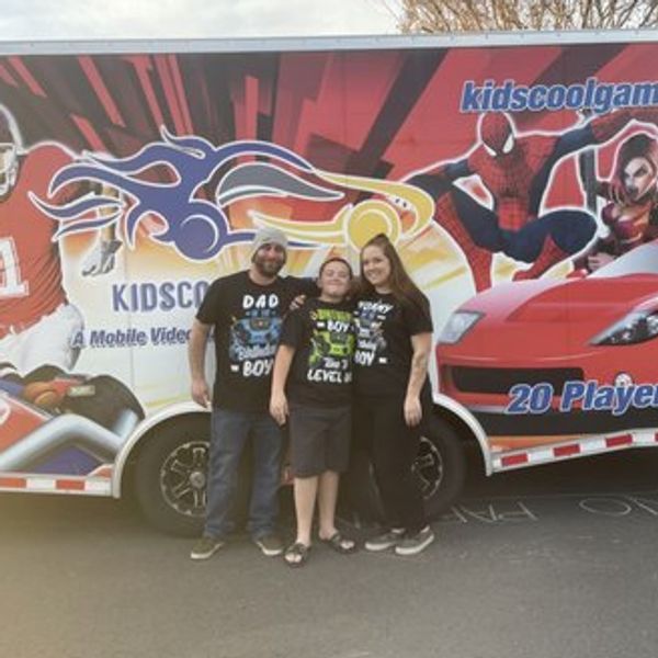 A family of three posing in front of a colorful mobile video game truck.