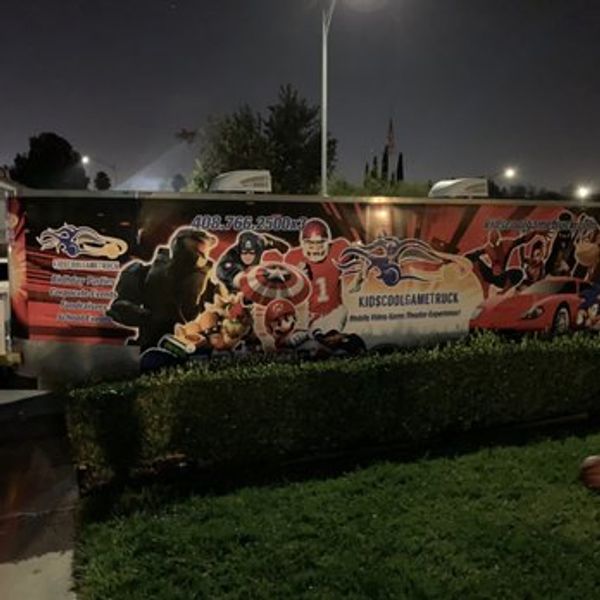 Colorful kids game truck trailer at night with superhero and sports graphics.