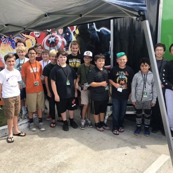 Group of boys posing outdoors near a colorful mural under a canopy.