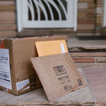 Delivered packages including a cardboard box and kraft mailer on a stone doorstep.