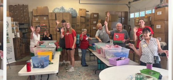 Group of people smiling and waving in a workspace filled with boxes and tables.