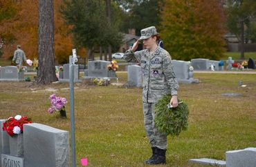 A soldier salutes as she places a wreath on the grave of a Veteran.