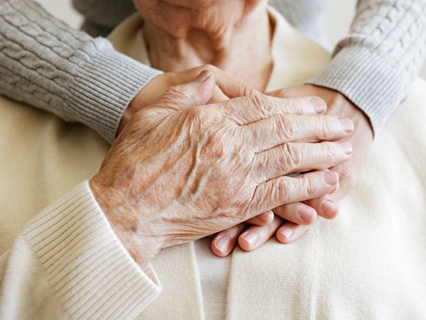 Mature woman in aged care facility receiving help from hospital staff nurse.