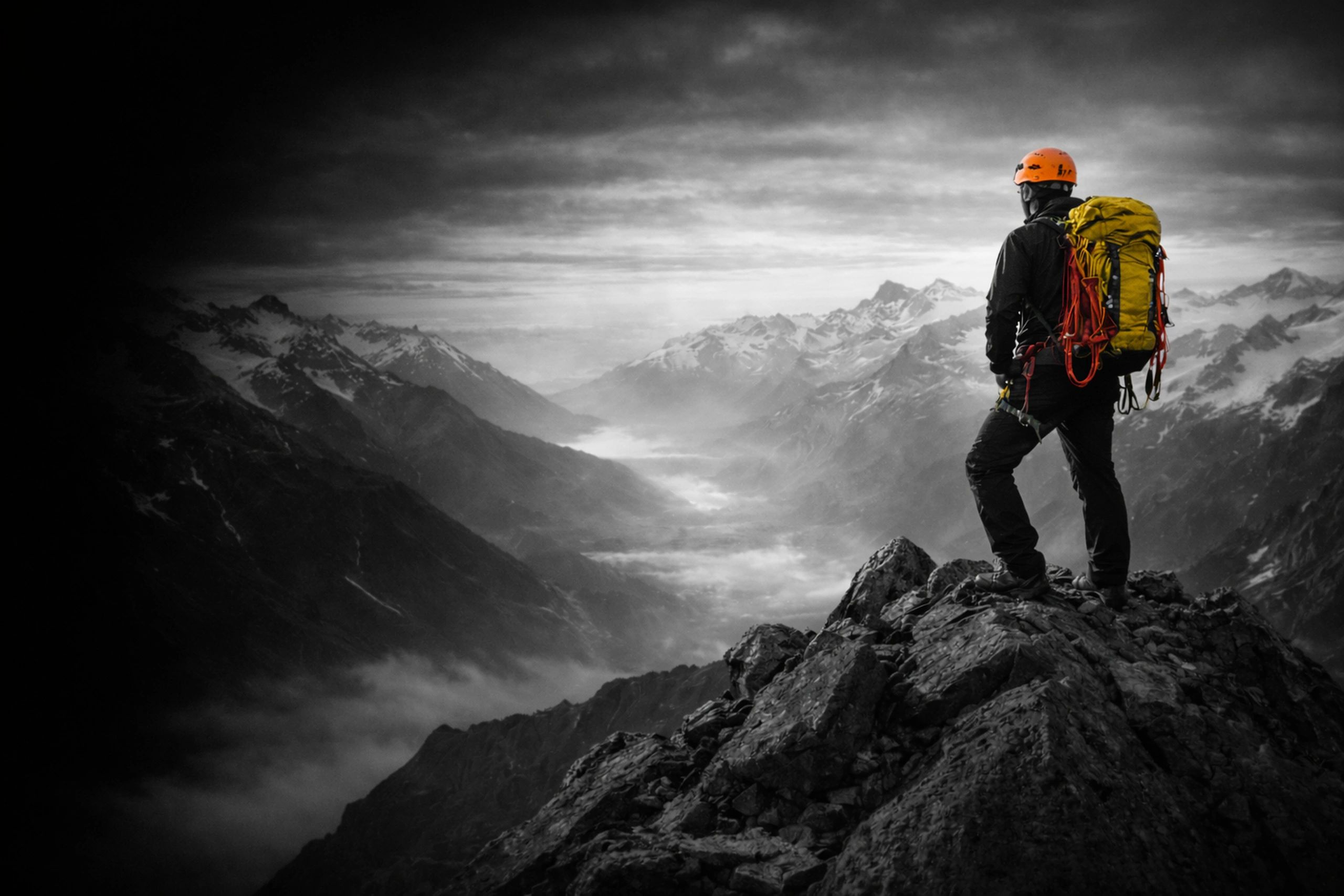 Climber stands on rocky peak overlooking misty mountain valley at dawn.