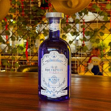 A blue bottle of Equanimity Tequila Blanco on a wooden table.