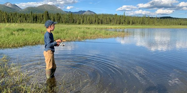Boy fishing in a lake surrounded by mountains and trees.