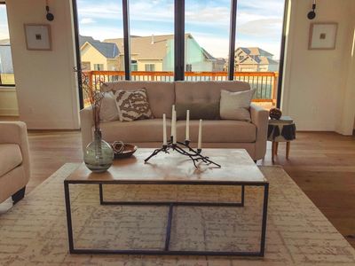 Cozy living room with beige sofa, modern coffee table, and large windows overlooking a sunny neighborhood.