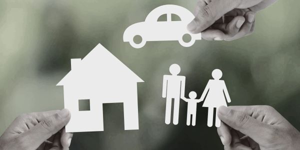 Hands holding paper cutouts of a house, family, and car symbolizing protection.