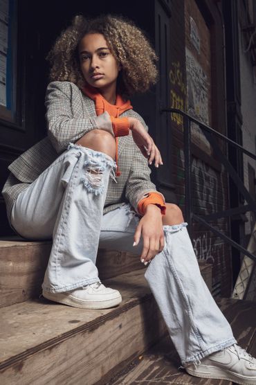 Teen model hanging out on Soho stoop. Wearing plaid blazer with orange hoodie and jeans
