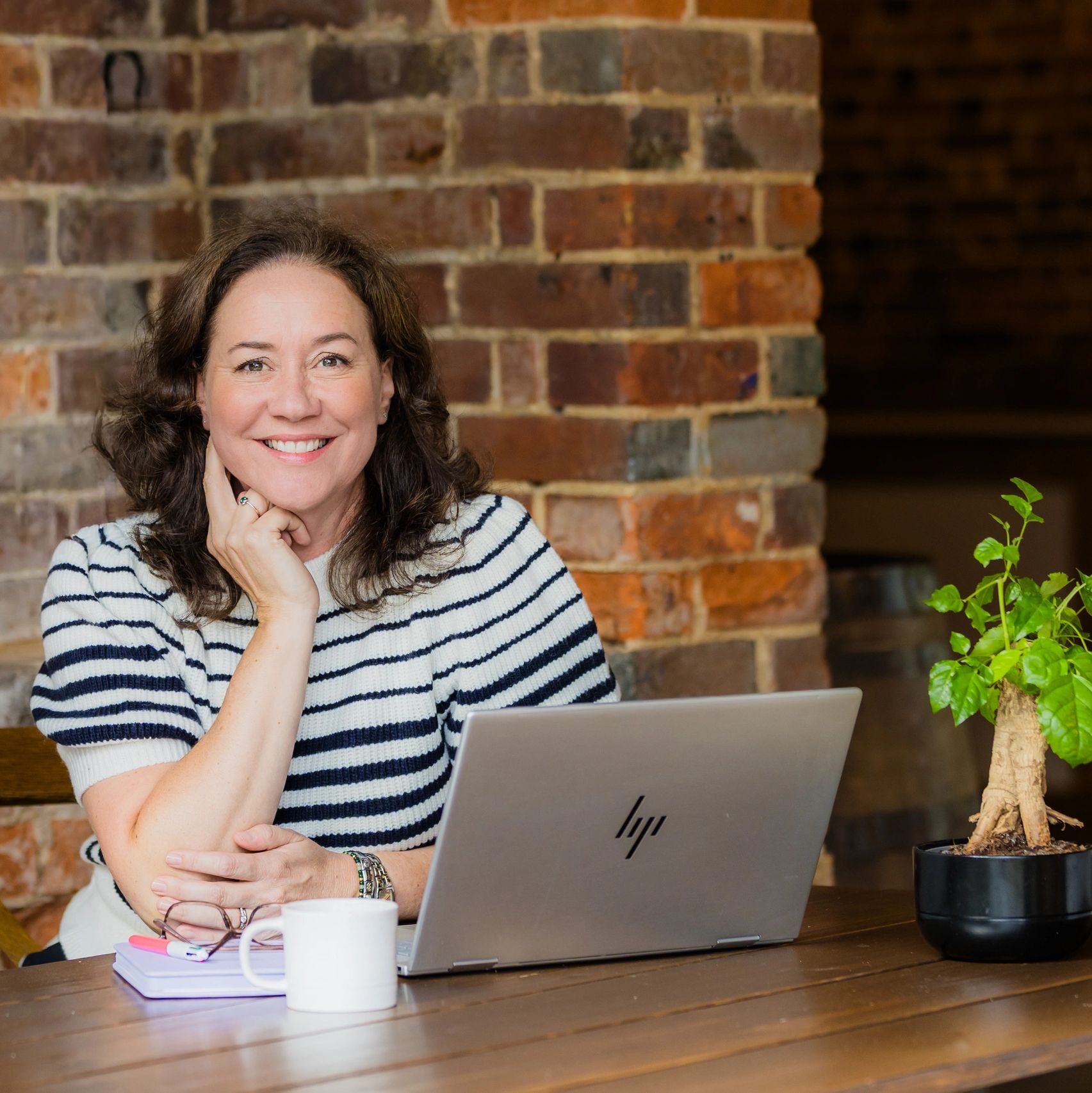 Founder smiling behind a desk with a laptop, cup and plant in shot