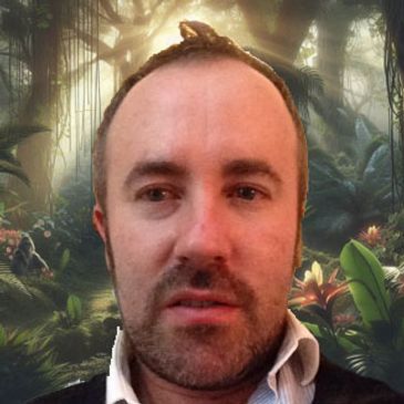 A man with a receding hairline in a lush forest setting.