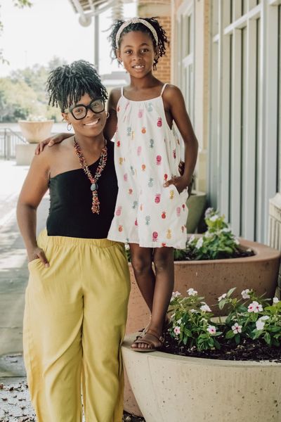 Smiling woman and girl posing outdoors by flower pots.