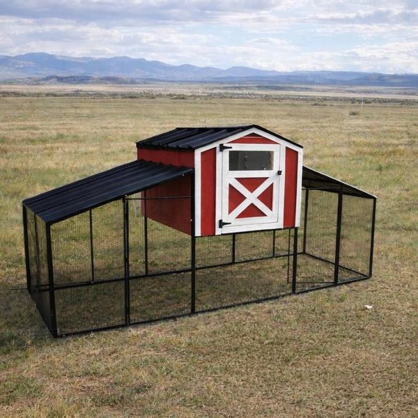 Red and white chicken coop with black roof in open field.