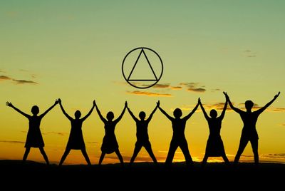 Group of people with arms raised and holding hands under the AA logo
