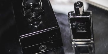 Black perfume bottle and skull-decorated box on reflective surface.