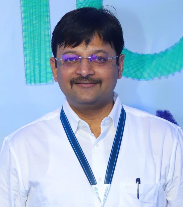 Man wearing glasses and a white shirt with an ID badge smiles at the camera.