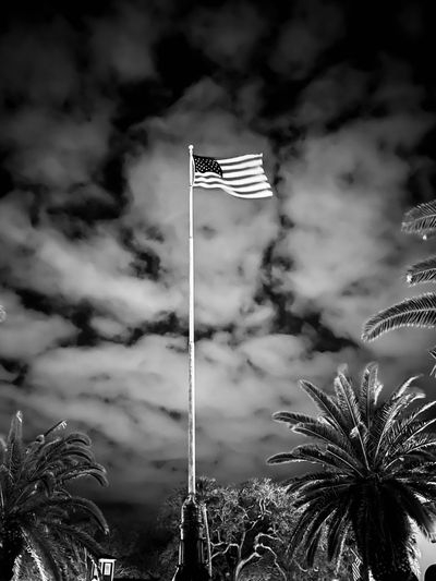 American flag waving atop a tall flagpole against a cloudy night sky.
