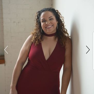 Smiling woman in a burgundy jumpsuit leaning against a white wall.