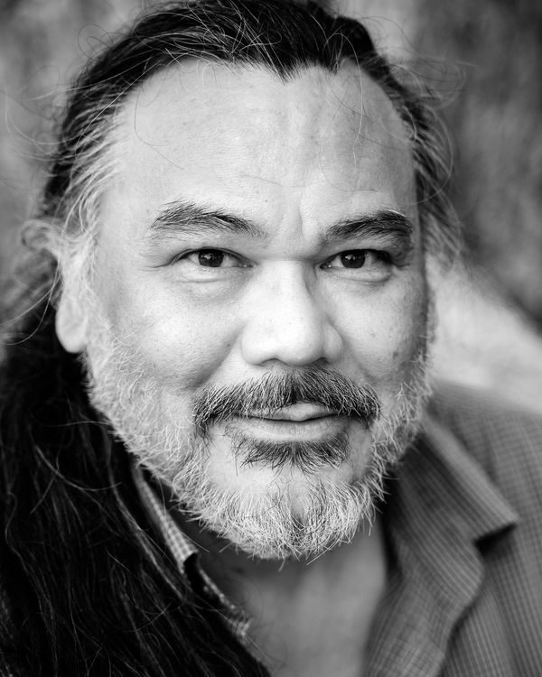 Close-up black and white portrait of a smiling bearded man with long hair.