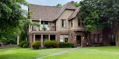 Historic two-story brick house with a large porch and green lawn.