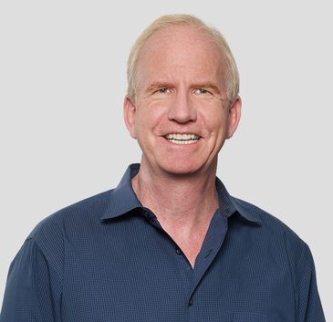 Smiling middle-aged man in a blue shirt against a plain background.