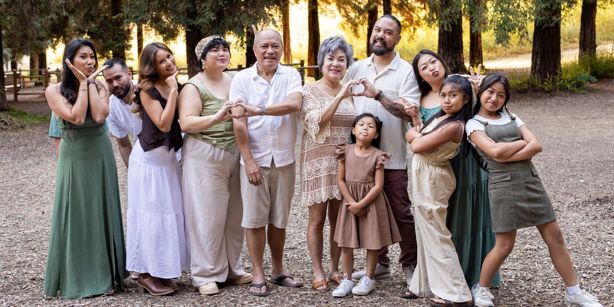 Large family posing playfully outdoors among trees.