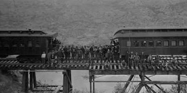 Two trains stopped on a railway bridge with people standing between.