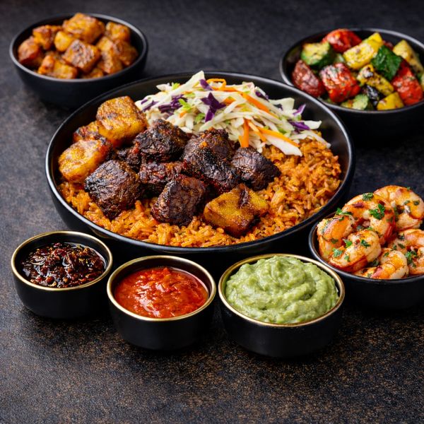 A vibrant African meal with jollof rice, grilled meat, plantains, shrimp, and sauces.