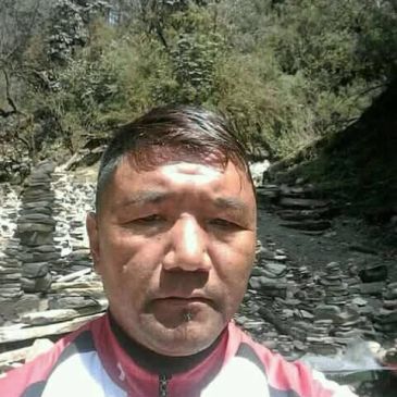 Man posing outdoors near a stone path.