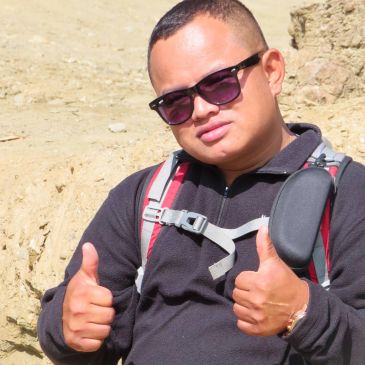Man giving thumbs up wearing sunglasses and backpack.