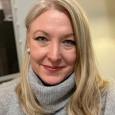 Smiling woman with blonde hair wearing a gray turtleneck sweater.
