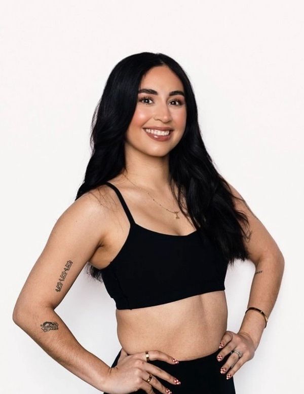 Smiling woman in black crop top with tattoos on her arms.