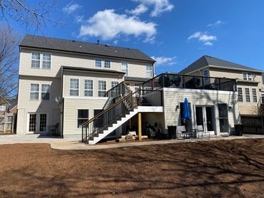 Large two-story house with a spacious backyard and elevated deck under a clear blue sky.