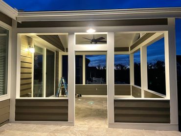 A well-lit, modern outdoor patio area at dusk with a ceiling fan and ladder.