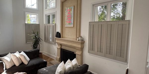 Modern living room with gray sofas, white pillows, and half-shuttered windows.