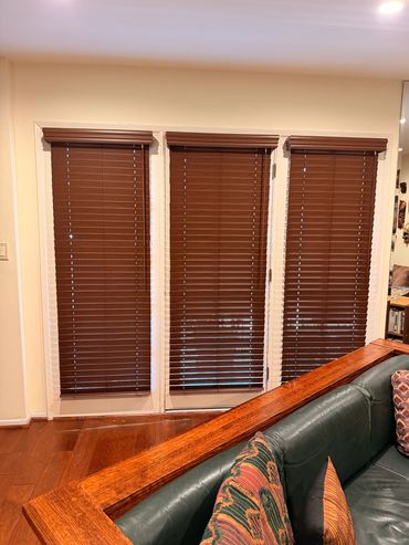 Brown horizontal blinds fitted across three tall living room windows.